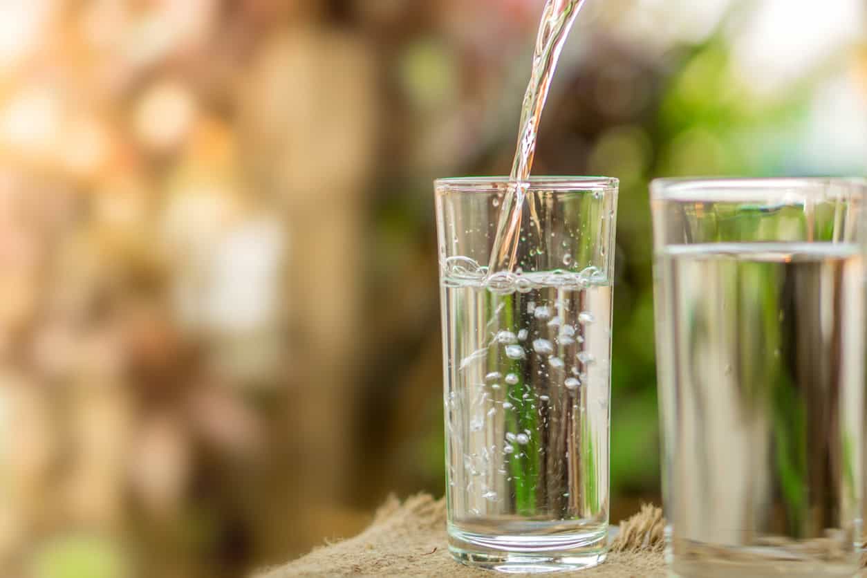 Clear glass cup being filled with water next to a filled glass cup of water