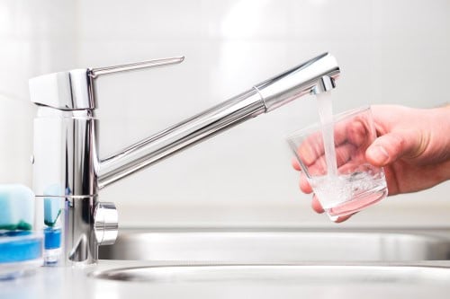 A person holding a glass under the faucet and filling it with water