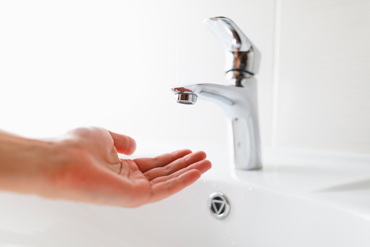 a person having their hand under a faucet without water