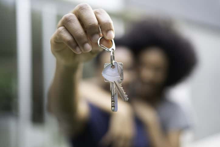 Young couple in front of a house, holding keys of their new home