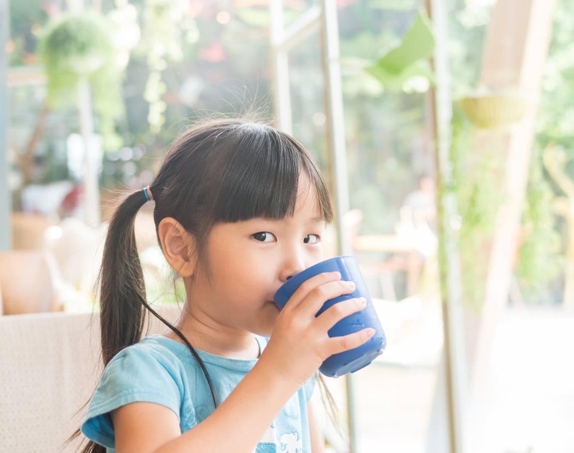 Asian girl child drink some water from the blue glass