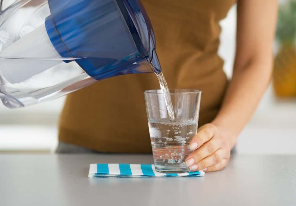 Women pouring water out a water filtration jug into a clear glass cup