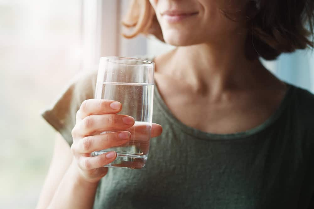 Women standing next to a window holding a clear glass cup filled with water