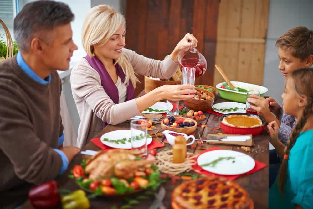 A family sitting at the dinner table and the mom pouring juice in a clear glass cup