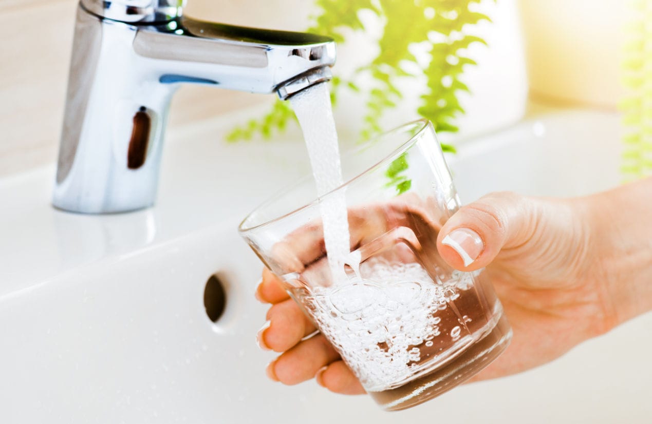 Hand holding glass getting clean drinking water from faucet, a black water softener system