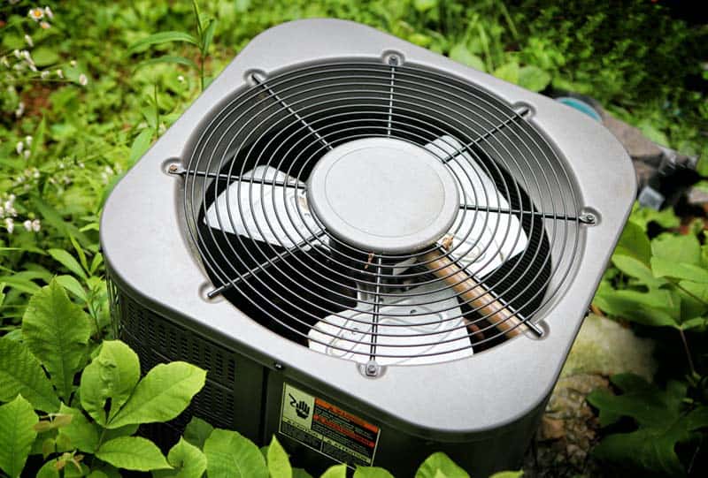 Air conditioner surrounded by grown greenery