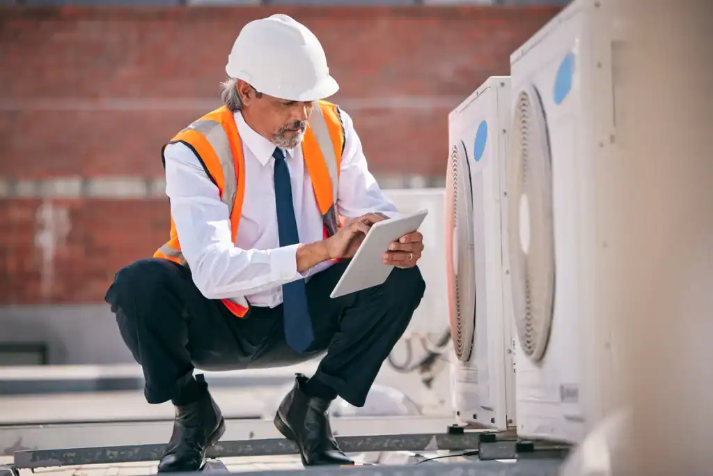 a man in a hard hat and vest squatting next to a device