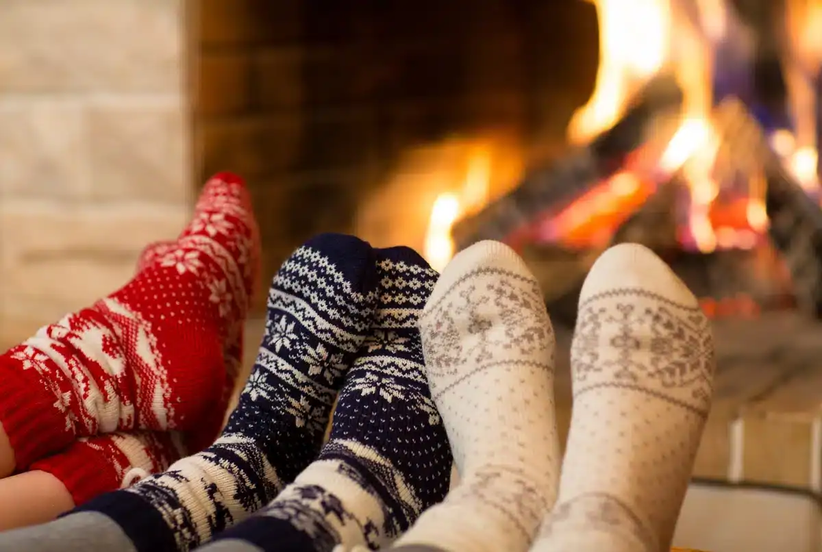 three people wearing socks warm their feet by the fire