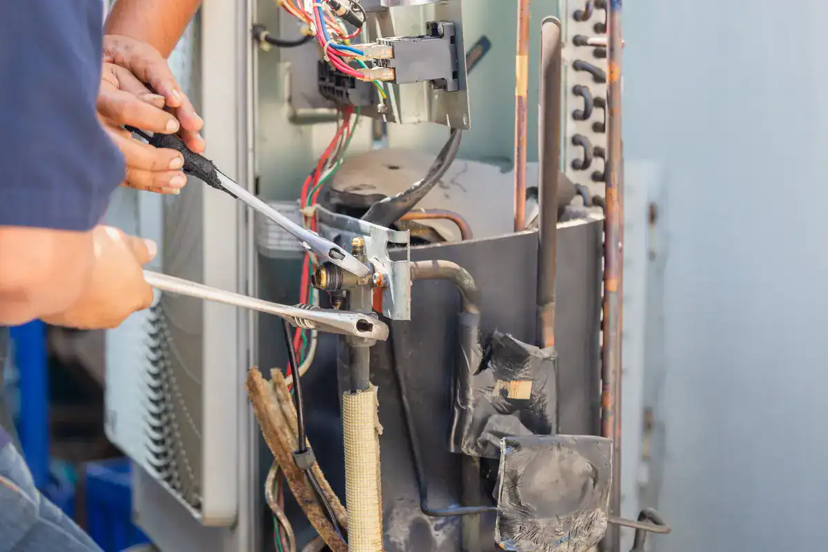 Two people are skillfully working on an air conditioning unit, using pliers and other tools to fix the intricate electrical wiring. As they navigate the colorful wires, their expertise in HVAC systems is evident, making them the go-to choice for anyone searching