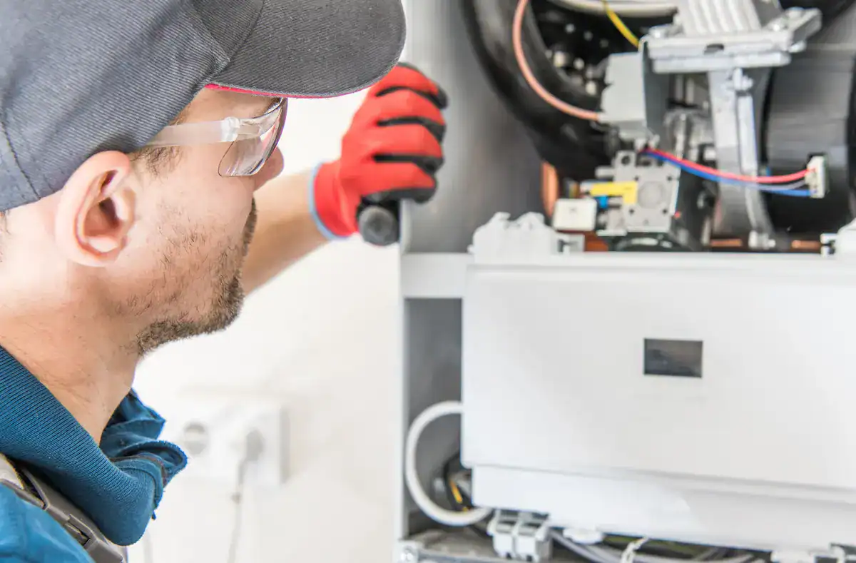 A technician in a cap and safety glasses is meticulously working on the internal components of an HVAC unit in Bemidji. He is wearing red gloves, closely examining parts to ensure everything operates smoothly.