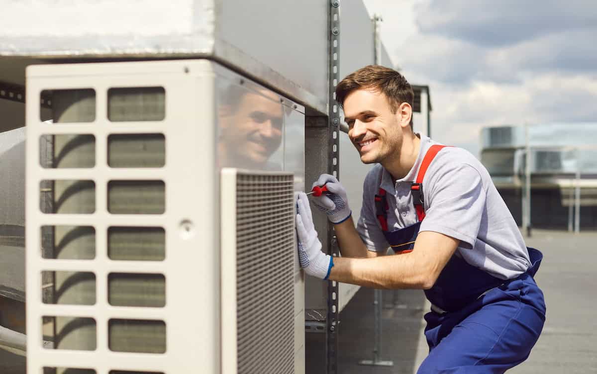 Young Repairman Installing And Repairing Ventilation System And Air Conditioner On The Rooftop.
