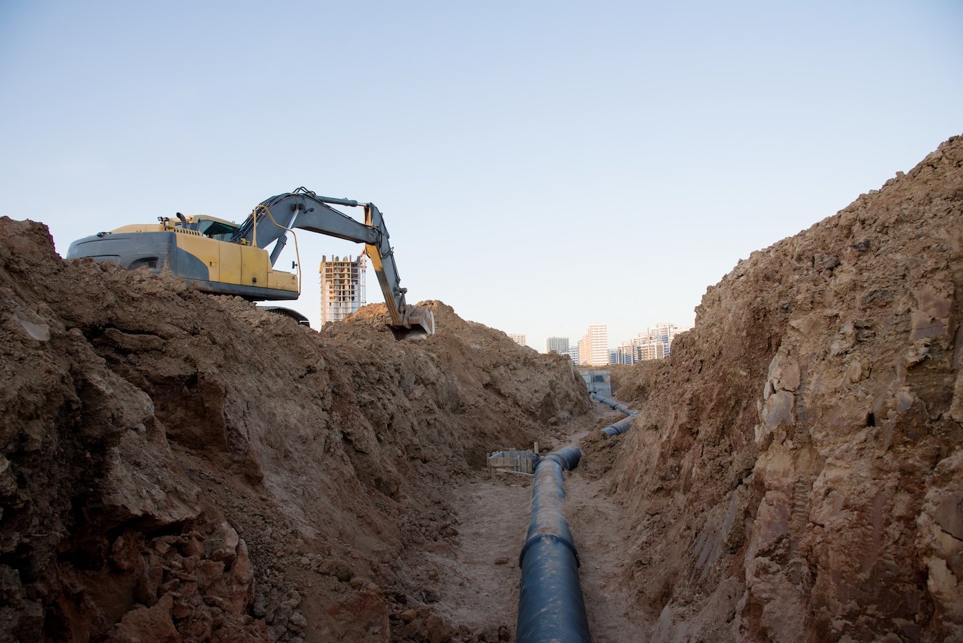 Excavator At Work Trenching At A Construction Site. Trench For Laying External Sewer Pipes. Sewage Drainage System For A Multi Story Building. Civil Infrastructure Pipe, Water Lines And Sanitary Storm